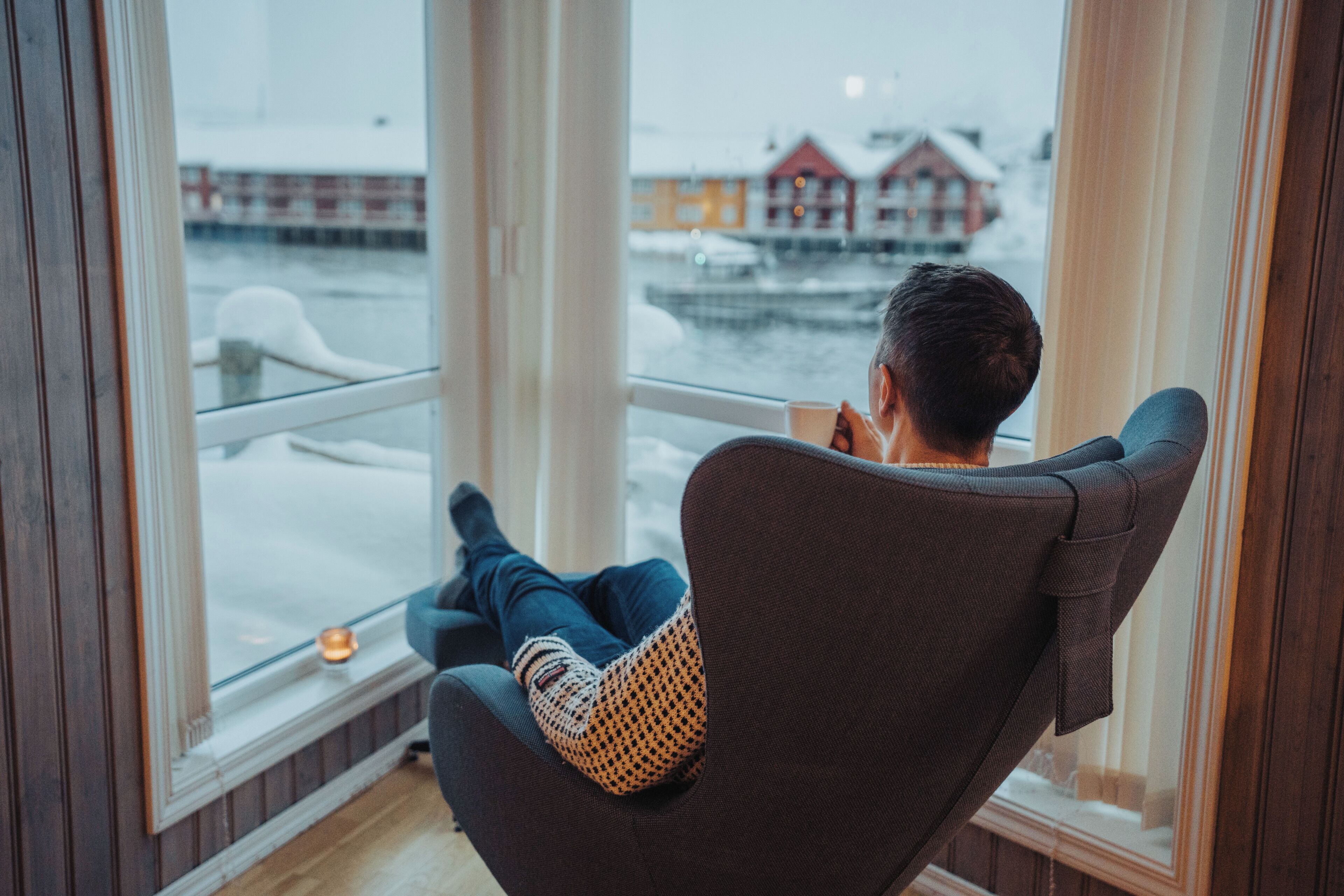 A person sitting in a chair by a window with a view of a harbor and buildings.