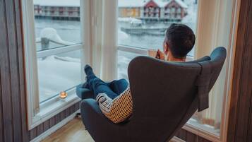 A person sitting in a chair by a window with a view of a harbor and buildings.