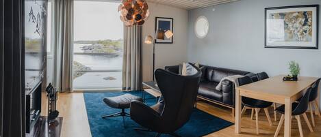 A modern living room with a sofa, a dining table, and a large window overlooking a body of water.