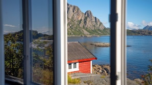 A coastal view with a red building, rocky shoreline, and mountains in the background. - Svinøya Rorbuer (Vagan)