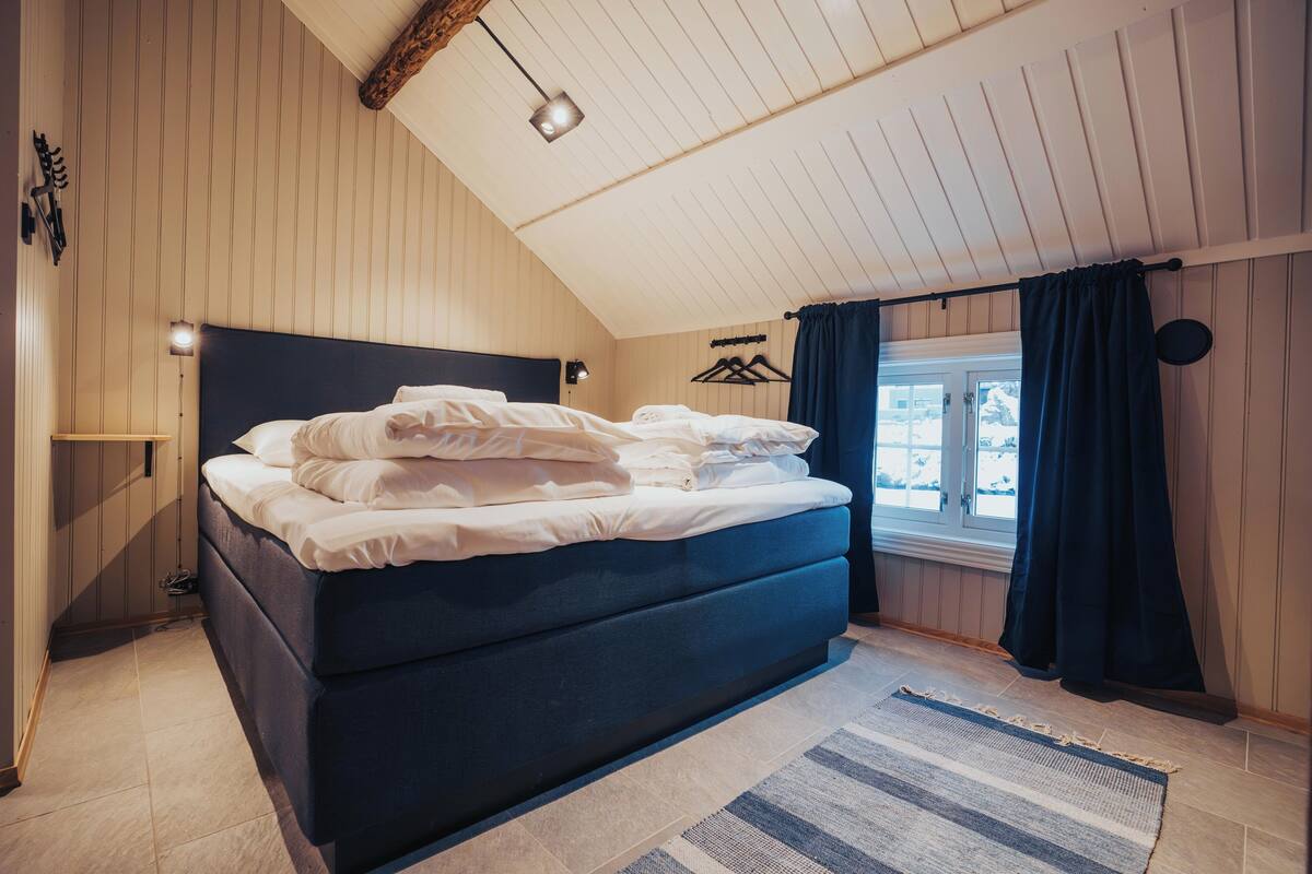 A bedroom with a bed, a window, a hanging light, and a wooden ceiling.