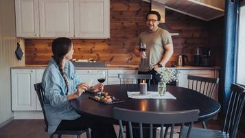 A cozy kitchen with wooden walls, a round dining table, and a person holding a glass of wine.