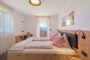 Une chambre à coucher avec un lit en bois, un bureau, une chaise, une fenêtre avec des rideaux et un tableau accroché au mur.