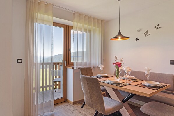 Un coin repas avec une table dressée pour deux personnes, une porte-fenêtre coulissante donnant sur un balcon et un luminaire suspendu au-dessus de la table.