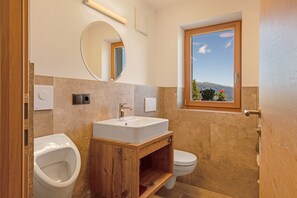 Une salle de bain moderne avec un meuble-lavabo en bois, un miroir rond, une fenêtre avec vue et des toilettes.