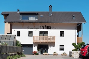 A two-story building with a balcony, a sign reading 'living lerchna,' and a red car parked in front.