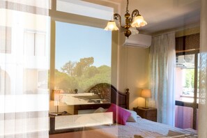 Un dormitorio con cama, mesitas de noche, lámpara, ventana con vistas y candelabro.