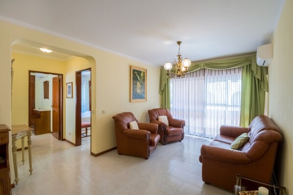 A living room with leather sofas, a chandelier, and a painting on the wall. - Apartment São Pedro do Mar with Terraces, A/C & Wi-Fi (Quarteira)