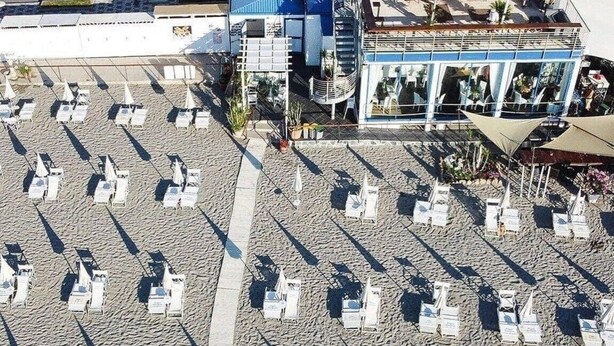 Un ristorante sulla spiaggia con posti a sedere all'aperto, un edificio blu e una palma sullo sfondo.