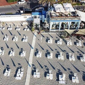 Un restaurant situé en bord de mer, avec une terrasse, un bâtiment bleu et un palmier en arrière-plan.