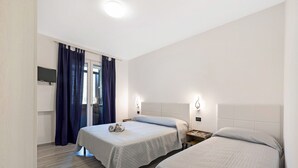 Una camera da letto con due letti, una TV a schermo piatto e una finestra con tende.