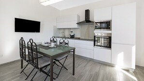 Una cucina moderna con mobili bianchi, una televisione a schermo piatto, un tavolo da pranzo con sedie e un forno a incasso.