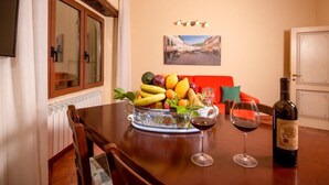 A dining table with a fruit bowl, two wine glasses, and a bottle of wine. - One Bedroom Apartment (Bibbiena)