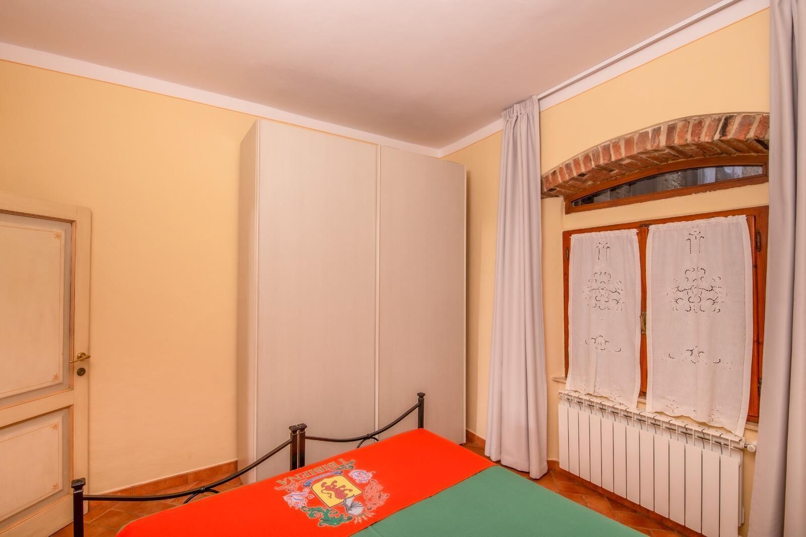 Ein Zimmer mit einem Bett, einem Heizkörper und einem Fenster mit Vorhängen.