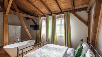 A bedroom with a sloped ceiling, a bathtub, a bed with green pillows, and a white cabinet.
