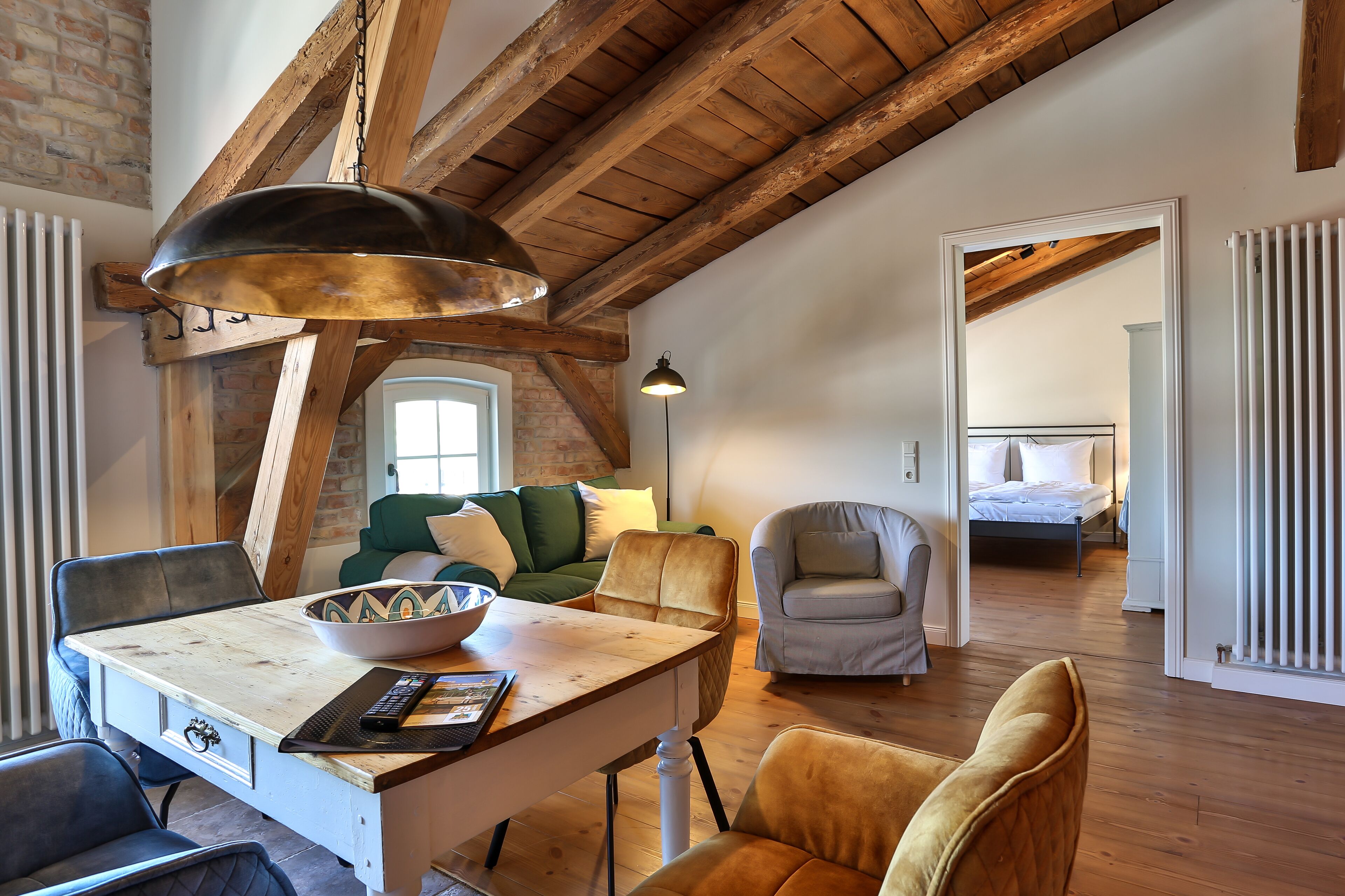 A cozy living room with a wooden ceiling, a dining table with a bowl and remote, a sofa, and a chair.