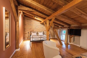 Un dormitorio con techo de madera inclinado, pared de ladrillo, cama, silla y televisor.