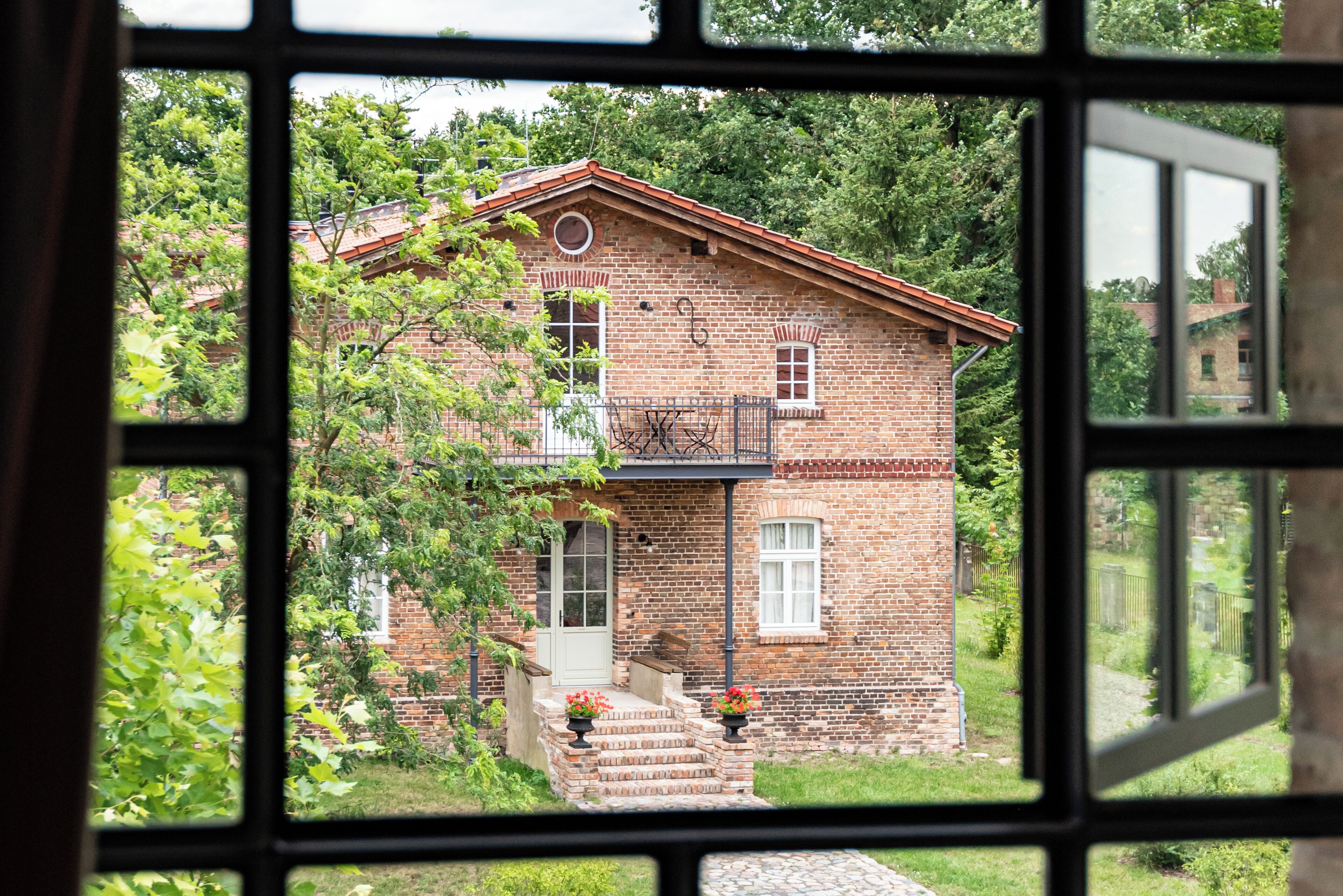 A brick house with a red roof, visible through a window with a grid pattern.