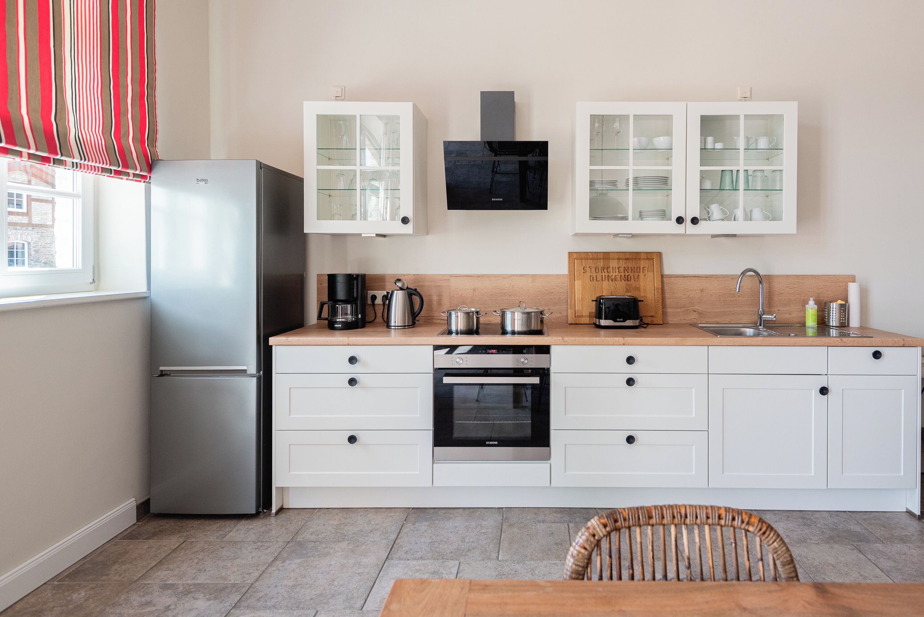 Una cocina moderna con armarios blancos, un refrigerador de acero inoxidable, horno empotrado y cafetera.