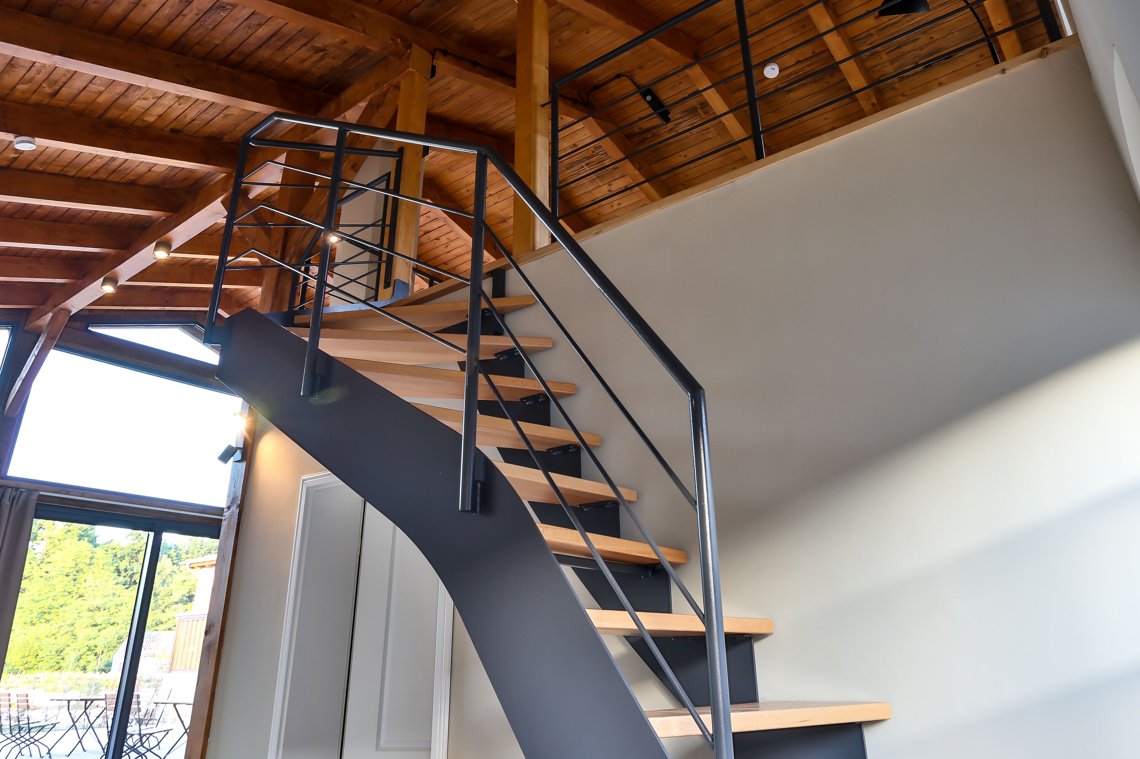 A modern interior with a curved staircase, wooden beams, and large windows.