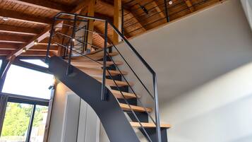Un interior moderno con una escalera curva, vigas de madera y ventanas amplias.