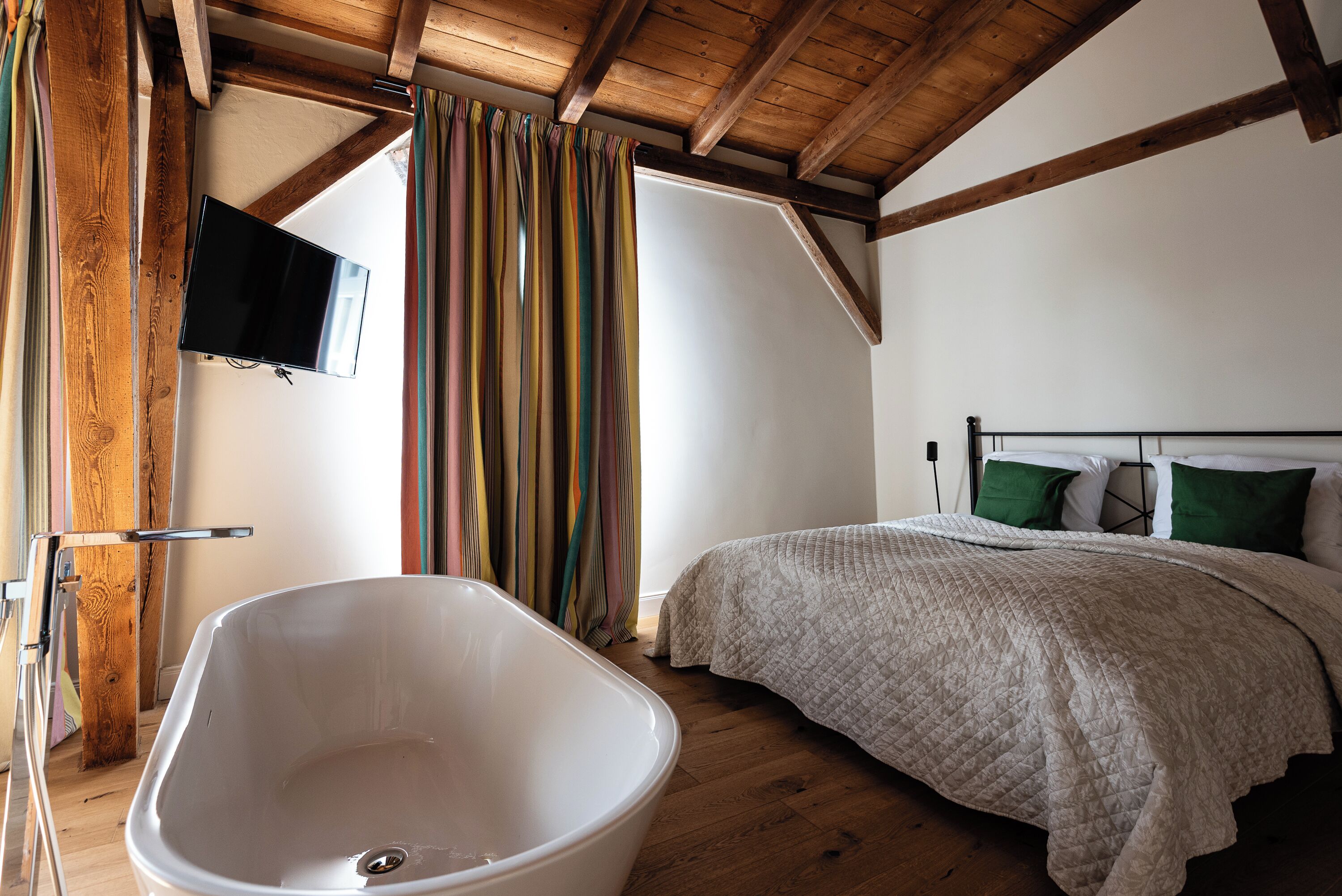 Un dormitorio con una bañera grande, una cama con almohadas verdes y un techo de madera.