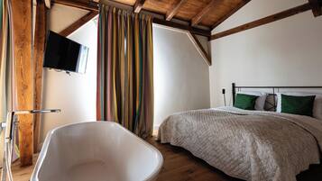 Un dormitorio con una bañera grande, una cama con almohadas verdes y un techo de madera.