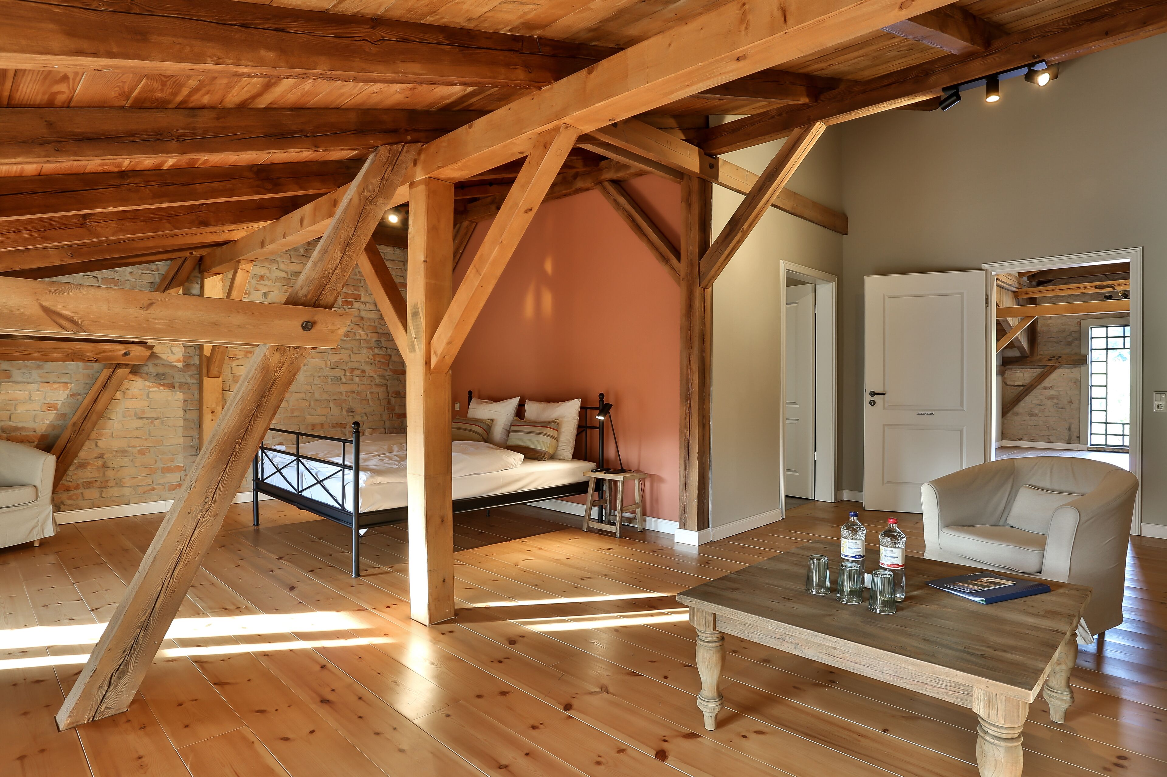 Un dormitorio tipo loft con vigas de madera a la vista, una cama, una silla y una mesa con botellas y vasos.
