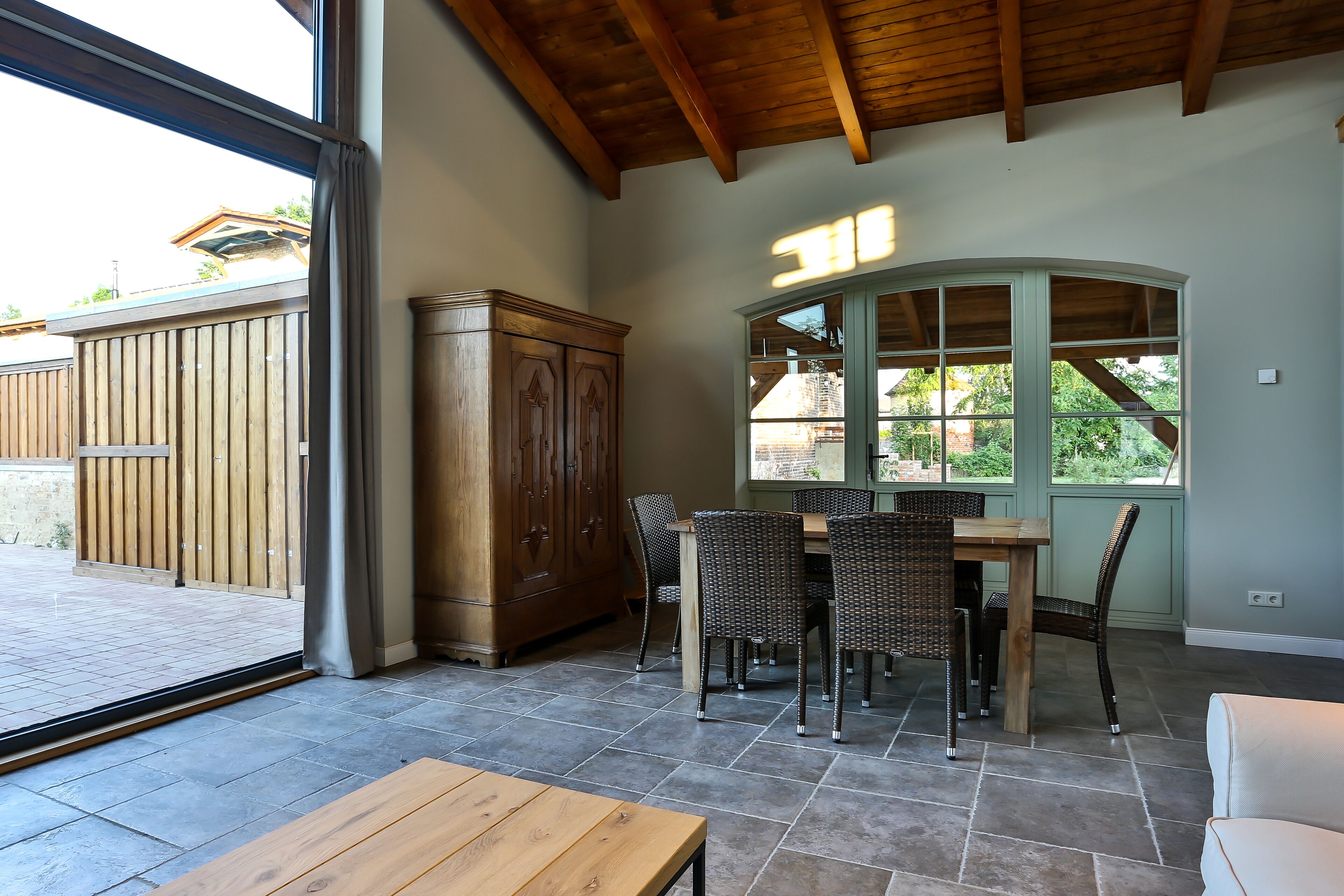Uma área de refeições com mesa e cadeiras de madeira, um armário e uma janela grande com vista para o exterior.