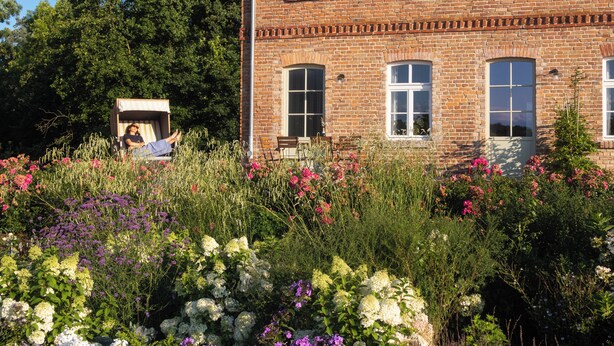 A brick building with multiple windows and a garden with various flowers. - Storchenhof Blumenow (Fürstenberg-Havel)