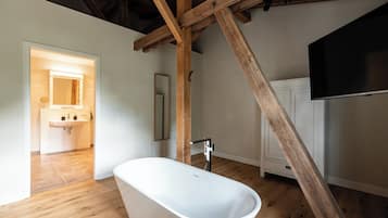 A spacious bathroom with a freestanding bathtub, wooden beams, and a large mirror.