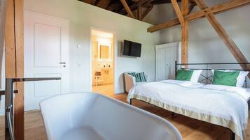 A bedroom with a large bed, a white bathtub, wooden beams, a television, and a door leading to another room.