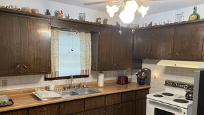 A kitchen with wooden cabinets, a white stove, a sink, and a window with curtains. - Pomme de Terre Lake Getaway: 5 Min walk to lake  – 15 Min drive to Lucas Oil (Hermitage)