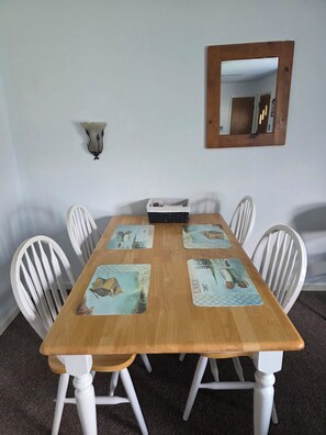 Una mesa de comedor con cuatro sillas, una mesita auxiliar de madera, un espejo montado en la pared y un aplique.