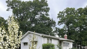 A white house with a chimney, surrounded by a well-maintained lawn and trees. - Pomme de Terre Lake Getaway: 5 Min walk to lake  – 15 Min drive to Lucas Oil (Hermitage)