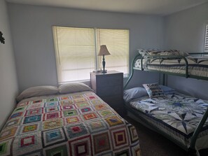 Une chambre avec des lits superposés, un lit recouvert d’une courtepointe, une commode et une lampe.