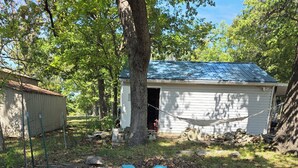 A fire pit surrounded by rocks, a hammock, and a shed with a blue roof. - Pomme de Terre Lake Getaway: 5 Min walk to lake  – 15 Min drive to Lucas Oil (Hermitage)