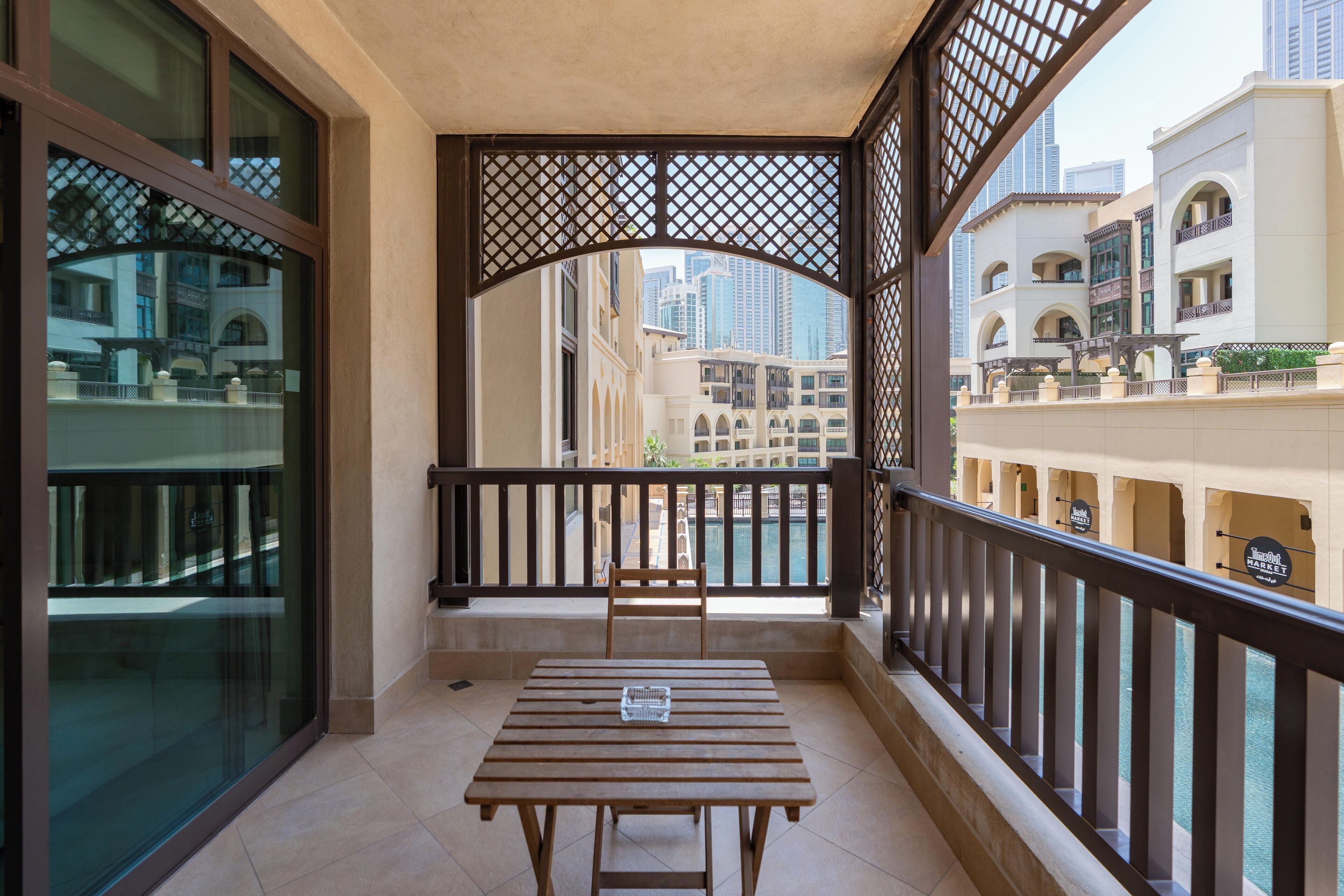 Un balcon avec une table et des chaises en bois, une porte vitrée et une vue sur des immeubles de grande hauteur.