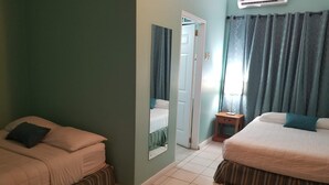 Habitación de hotel con dos camas, una mesita de noche pequeña, un espejo y una puerta que da a otra habitación.