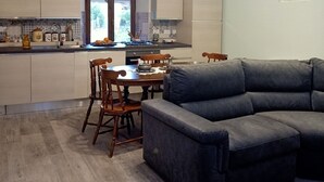 Une cuisine moderne avec un coin repas, comprenant un canapé d’angle gris, des chaises en bois et un lustre.