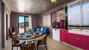 A modern kitchen with pink cabinets, a dining area with a round table, and a blue sofa. - Alki Slow Living - Alkinoe (Afandou)