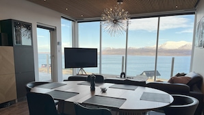 A modern kitchen with a large island, a dining area with chairs, and a view of a lake with mountains in the background.