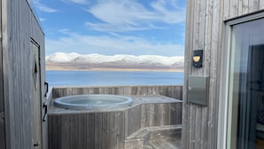 A wooden deck with a hot tub, a glass door, and a view of a lake and mountains.