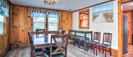 A dining area with a wooden table and chairs, a chandelier, and a painting of a beach scene.