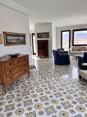 Een woonkamer met patroon vloertegels, een houten dressoir, een bank en een uitzicht door grote ramen.