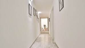 Een hal met betegelde vloer, ingelijste foto's aan de wanden en uitzicht op een balkon met een tafel en stoelen.