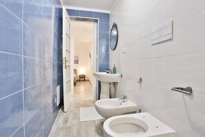 Ein modernes Badezimmer mit blauen und weißen Fliesen, einem Bidet, einem Waschbecken und einem Spiegel.