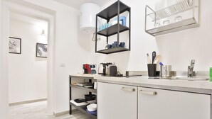 Een moderne keuken met witte kasten, een zwarte hangplank met servies, en een klein aanrecht met een koffieapparaat.