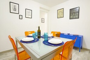 A dining area with a glass table, orange chairs, and framed artwork on the walls.