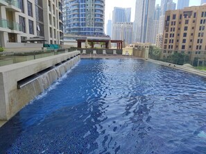 Una piscina en la azotea con una cascada, rodeada de edificios altos.